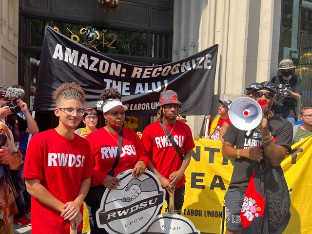 Chris Smalls, the president of the Amazon Labor Union, holds a megaphone as he addresses a crowd in front of Jeff Bezos’ house in Manhattan. He is standing in front of banners and is joined by Amazon workers attempting to unionize in Bessemer, Alabama.